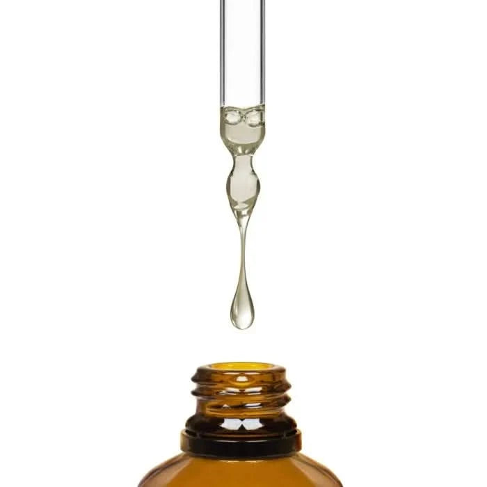 Glass dropper with a drop of liquid over an amber bottle on a white background