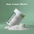 Container of brazen grass fed collagen creamer with powder and scoop on a green background